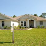 Beautiful suburban house with lush lawn, showcasing a for sale sign under a clear blue sky.