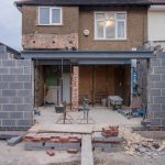 Brick house under renovation with an extension in progress. Visible construction site materials and structure.