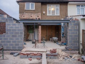 Brick house under renovation with an extension in progress. Visible construction site materials and structure.
