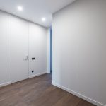 A minimalist indoor corridor featuring sleek doors and wooden flooring under bright lighting.